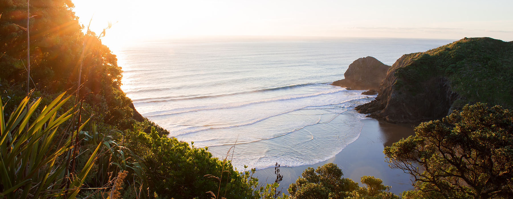 View of a small cove and beach from above with the sun setting out on the water