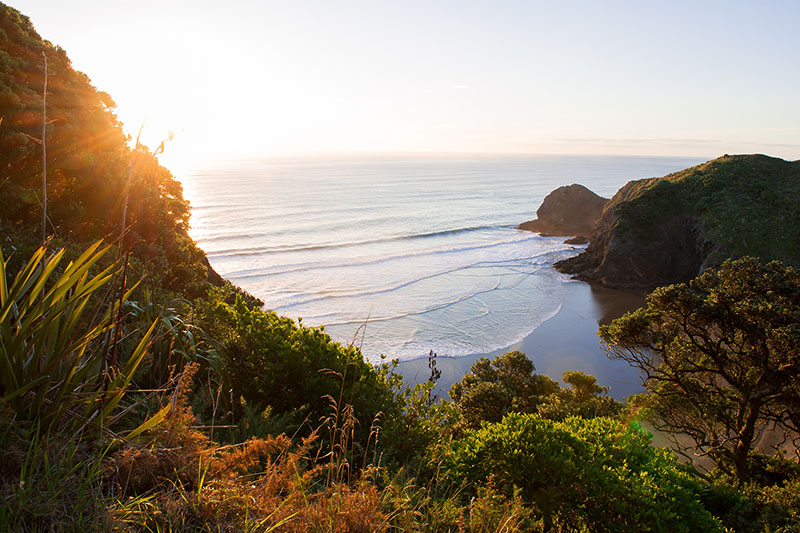 View of a small cove and beach from above with the sun setting out on the water