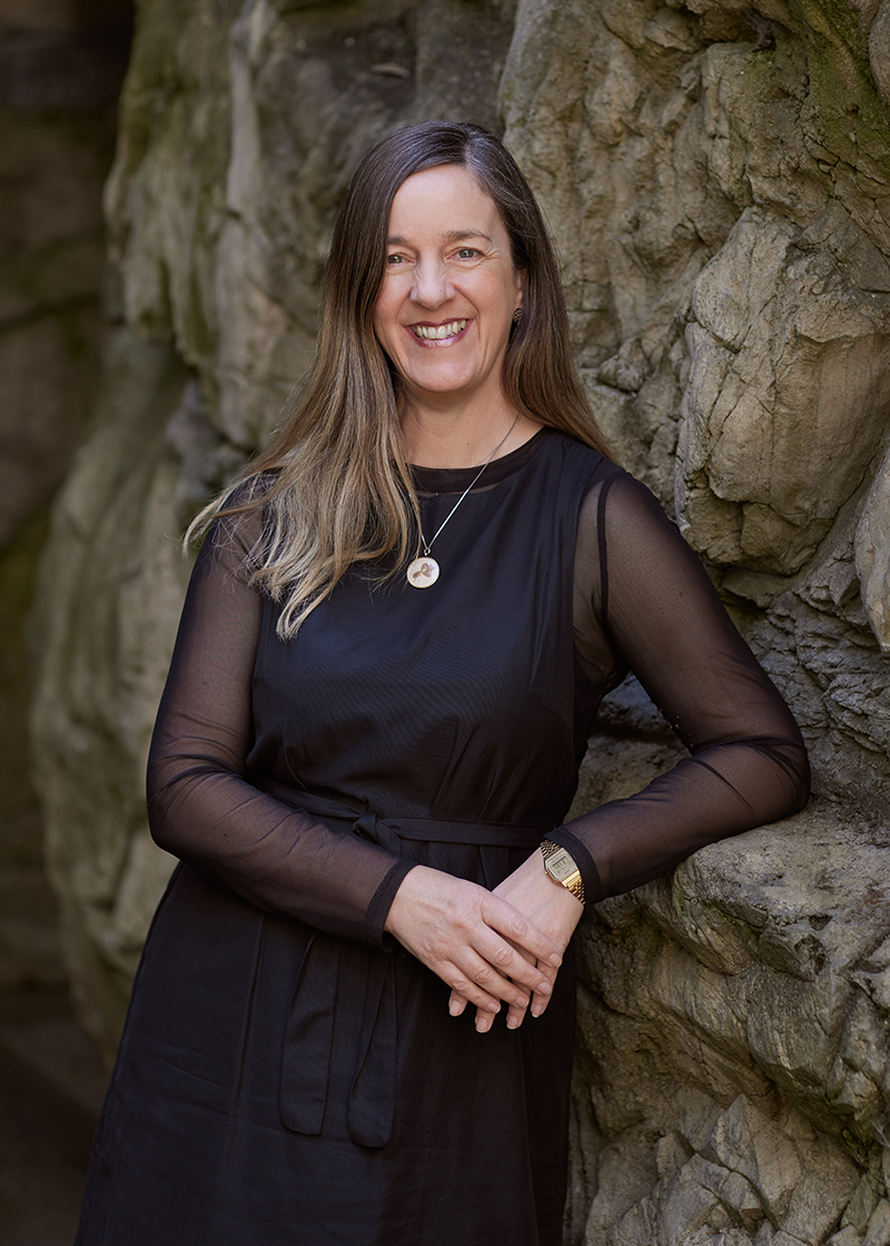 A photo of a woman in a black outfit leaning against a stone wall.