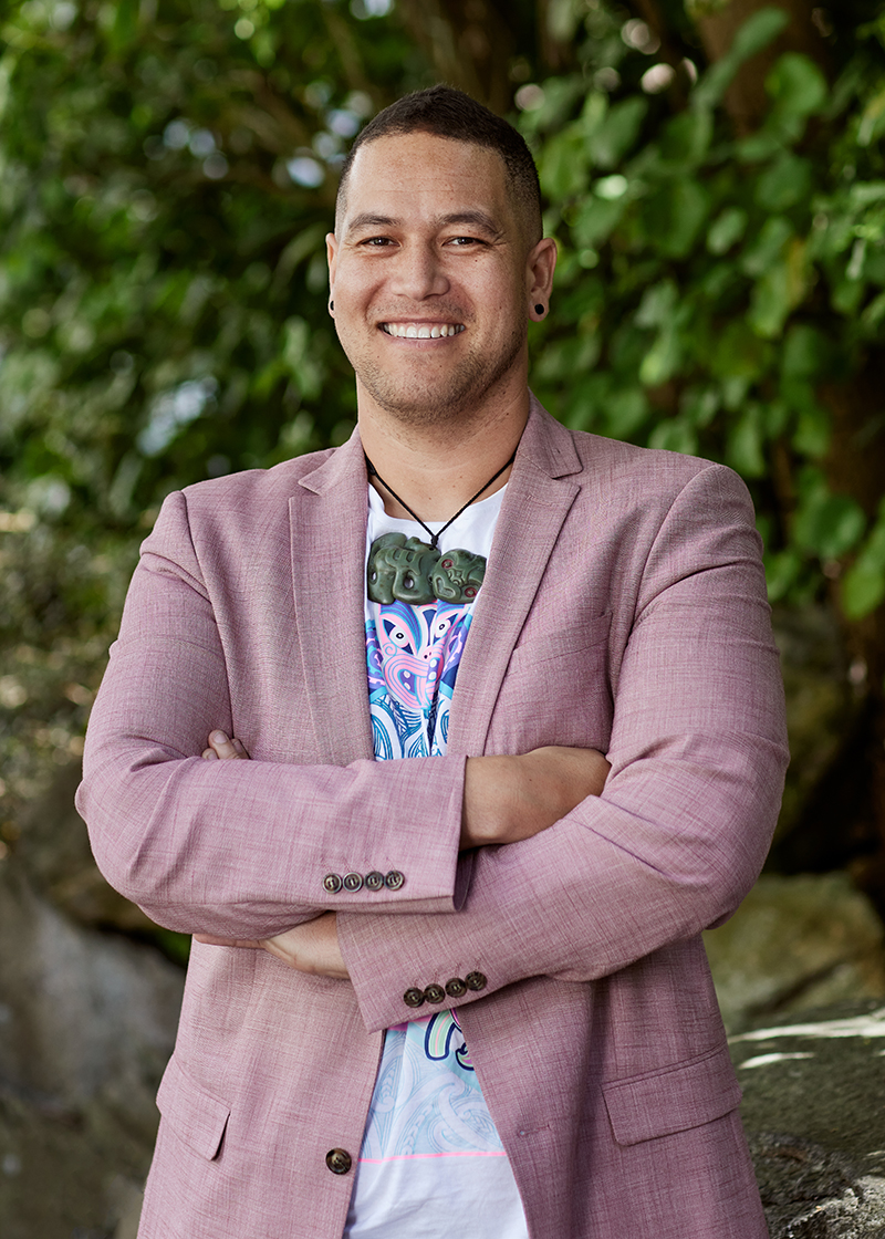 A man in a pink jacket and a t-shirt is smiling at the camera.