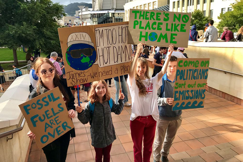 Four school children holding protest signs outside in a public square.