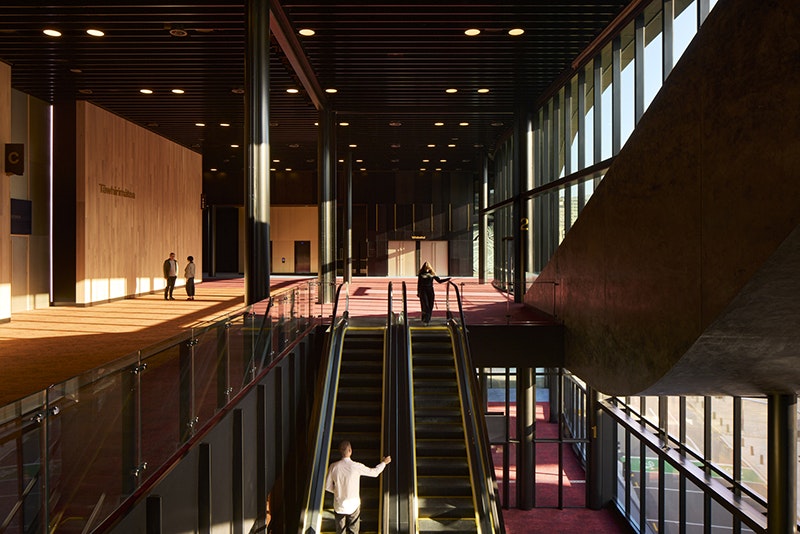 Inside a convention centre with escalators and people walking around.