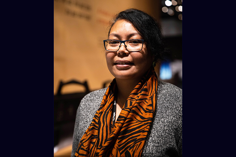 head and shoulders of a woman wearing an orange and black scarf. She has dark hair and is wearing glasses.