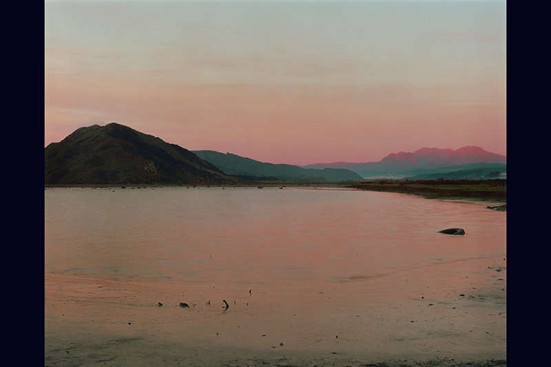 A photograph of a a sunset on the mouth of a river. The sunset is reflected in the smooth water.