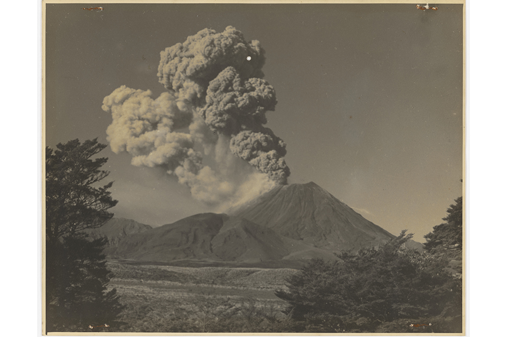 A black and white photo of a massive amount of smoke coming out of the top of a mountain.