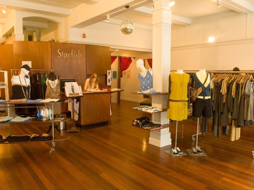 Image of the Starfish retail shop at 128 Willis Street, Wellington, November 2006, by Grant Maiden Photography. Gift of Laurie Foon, Starfish, 2014. © Te Papa. CC BY-NC-ND 4.0. Te Papa (CA001203/014/0004/0001/0015) A woman is behind the counter of a clothing store.