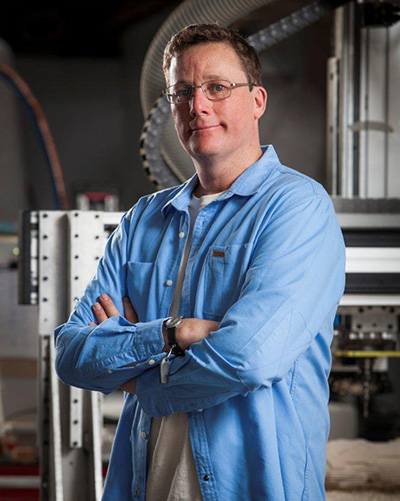 A man in a blue shirt with his arms crossed is looking at the camera.