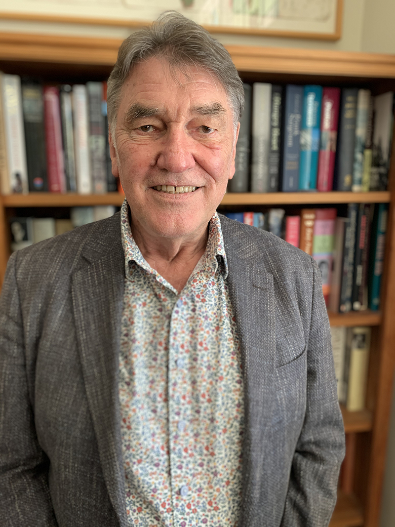 Top half of a man standing in front of a bookshelf and smiling at the camera.