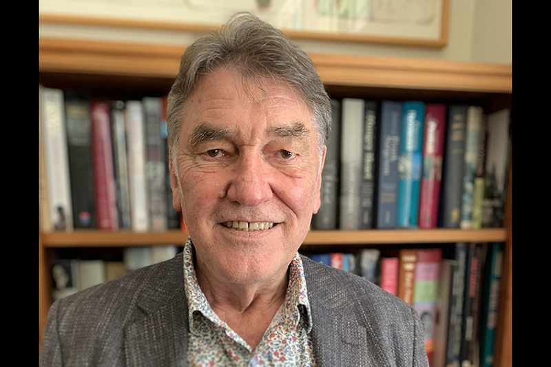 Top half of a man standing in front of a bookshelf and smiling at the camera.