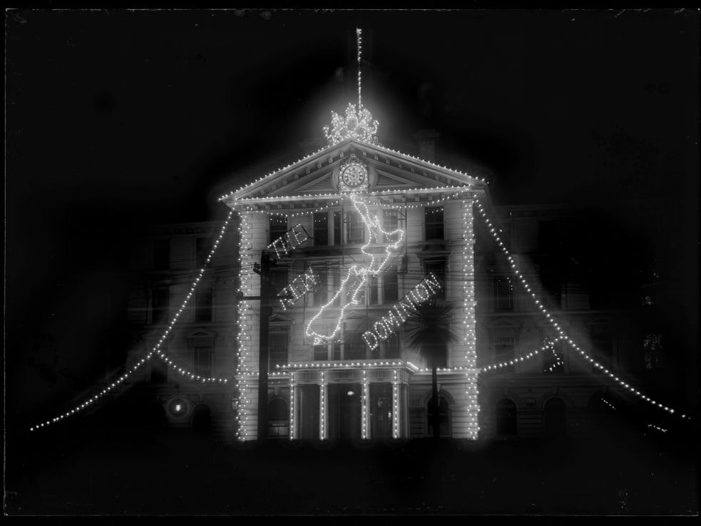 Dominion Day - Government Buildings at night Building lit up with small lights in the shape of New Zealand and the words The New Dominion.