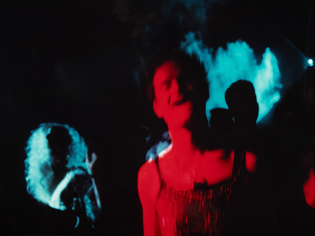 Giovanni, Hero Party, Auckland. 1994, Ann Shelton, 1994, cibachrome photograph. Chartwell Collection, Auckland Art Gallery o Tāmaki, 2008 A photo of someone dancing or singing at a darkly lit space with red and blue lighting.