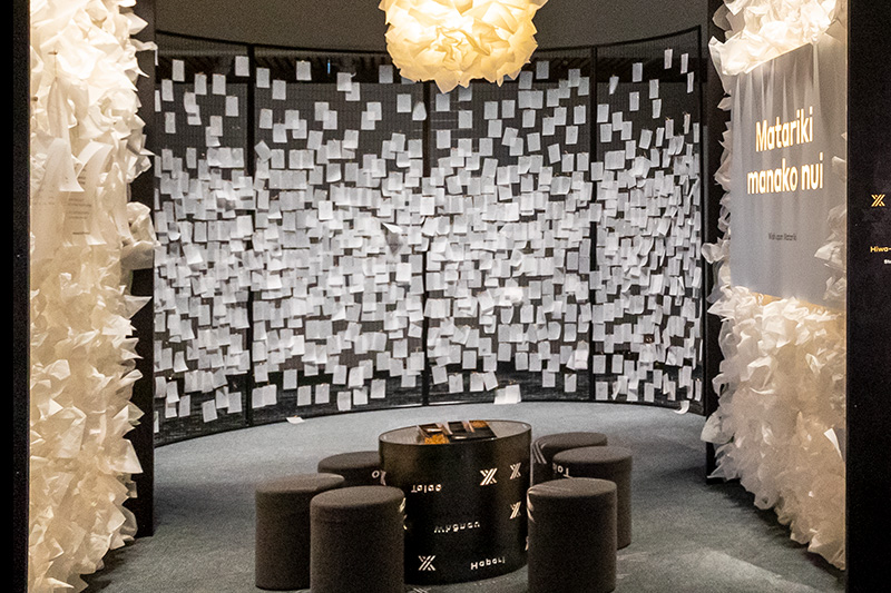 A wall of white paper notes tied on with gold string.