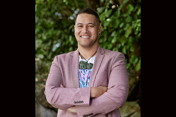A man in a pink jacket and a t-shirt is smiling at the camera.