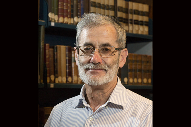 Head and shoulders of a man with a trim beard and glasses smiling sat the camera