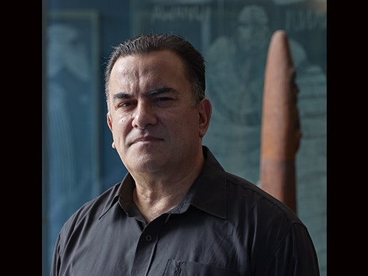 Sean Mallon. Photo by Yoan Jolly. Te Papa Head and shoulders of a man looking at the camera. He is half in shadow,