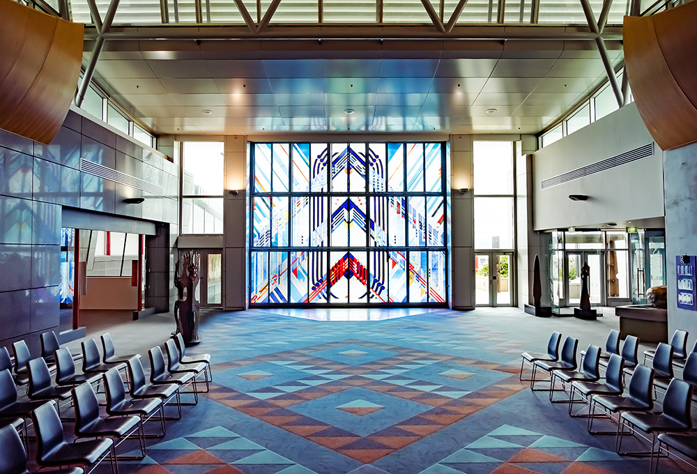 Carpeted area with chairs set out facing each other. There is a large stained-glass window at the back of the room and doors leading off from both sides.