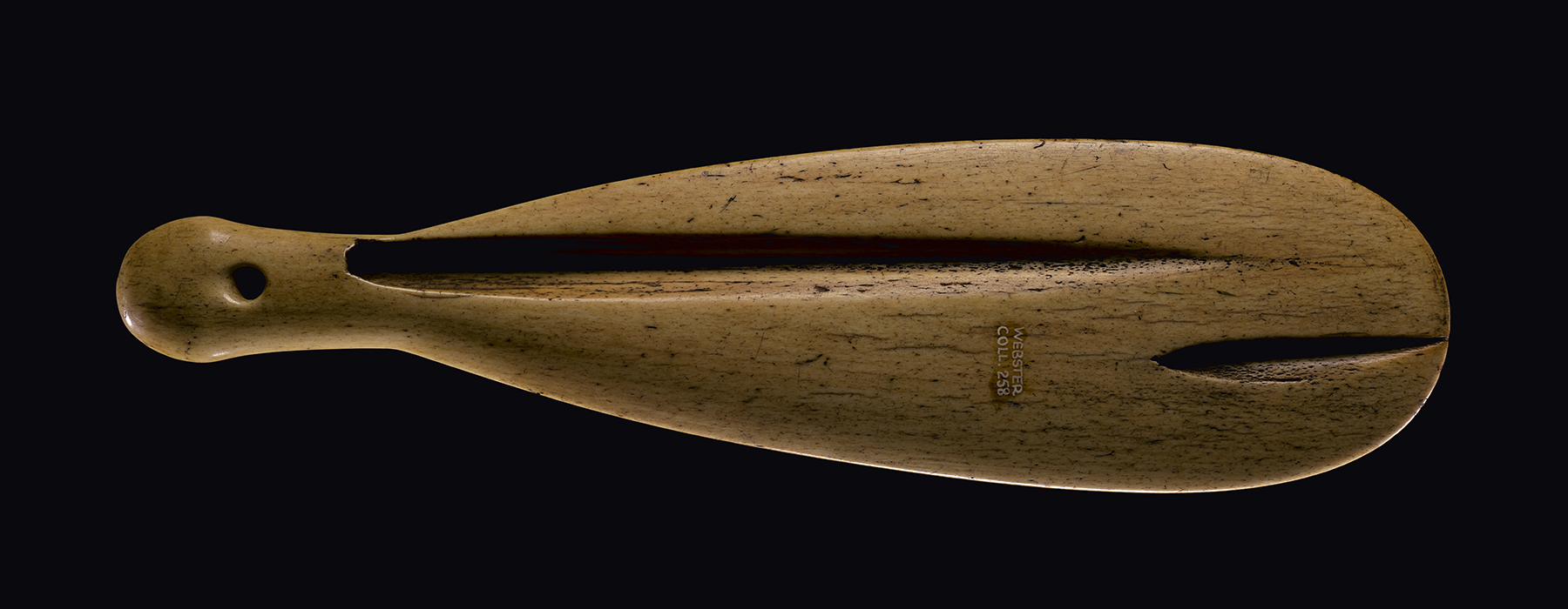 A brown whalebone club with two grooves in it on a dark background.