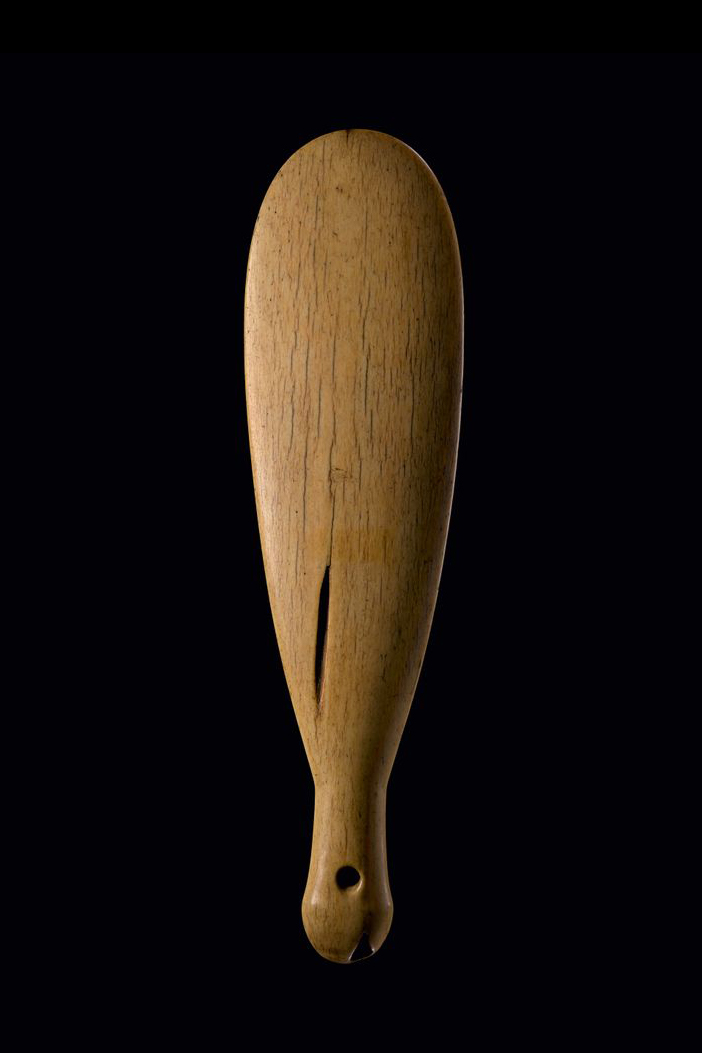 A brown whalebone club with two grooves in it on a dark background.