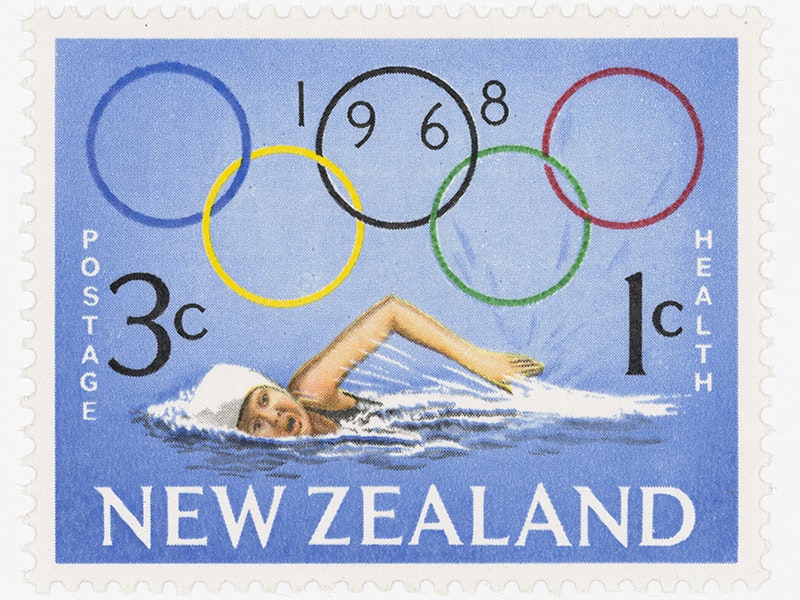 Issued three cent 'Olympic Games' Health stamp, Harrison & Sons Ltd.; printer; 1968; England. The New Zealand Post Museum Collection, Gift of New Zealand Post Ltd. 1992. Te Papa (PH001928) A stamp showing someone in a white swimming cap swimming through water. There are the Olympic rings above the person and the words Postage 3x, 1c Heath, the date 1968,  and the words New Zealalnd