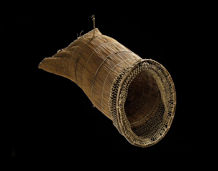 A woven net to catch fish or eels. It is sitting on a black background.