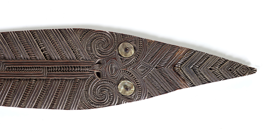 the tip of a wooden spear with intricate carvings and two paua shell 'eyes' are placed near the tip so it looks like a snake.