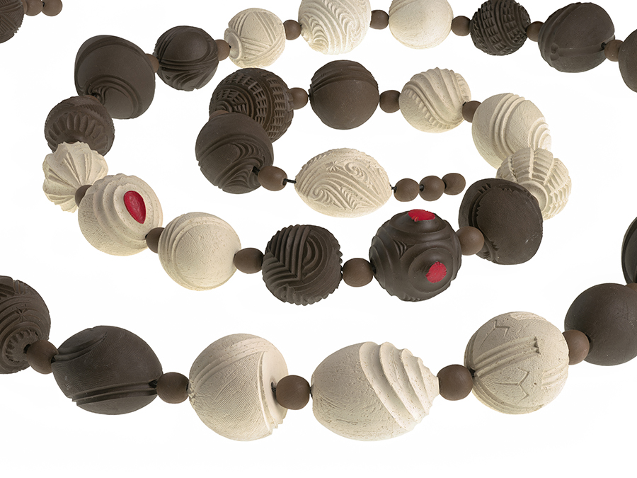 A string of clay beads in a coil. Some of the largerr beads are dark brown clay, some are white, and somc of them have red dots on them.