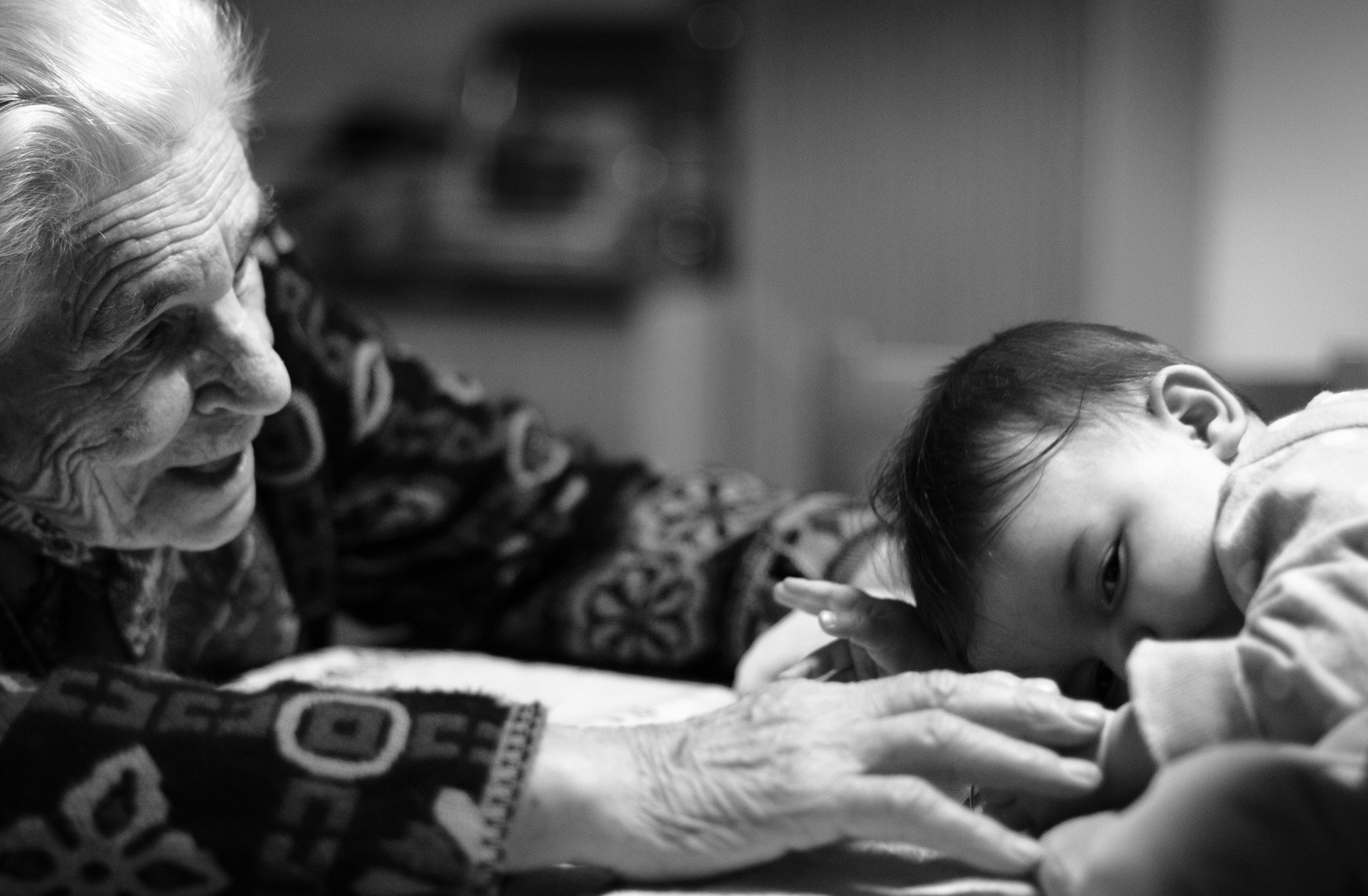 An elderly woman is reaching out to a small baby child who is lying on its stomach.