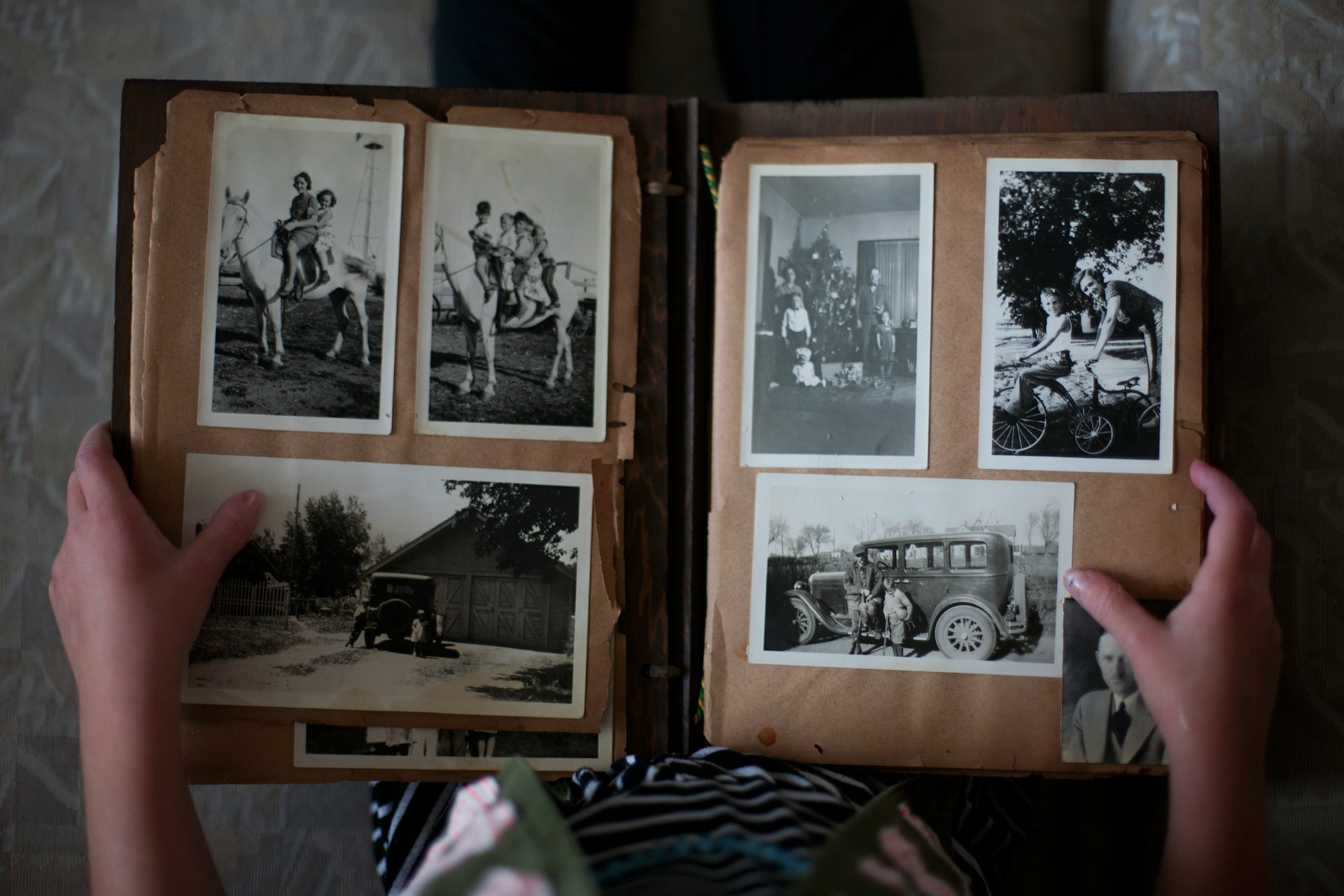 a top-down photo of an open photo album with six black and white photos of people in the page spread. There are two hands holding the album open.