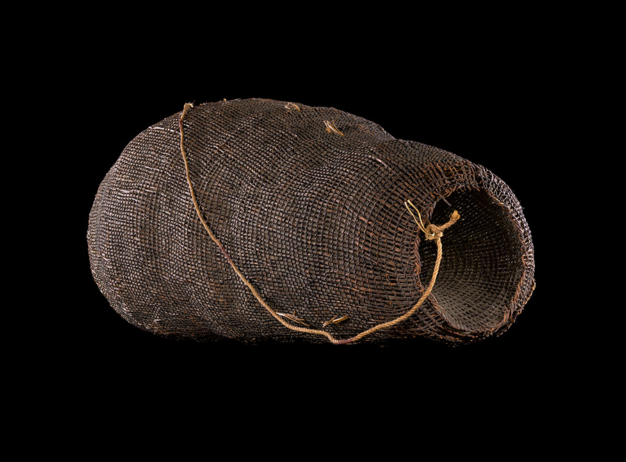 A woven basket with a plaited handle sitting in a black background.