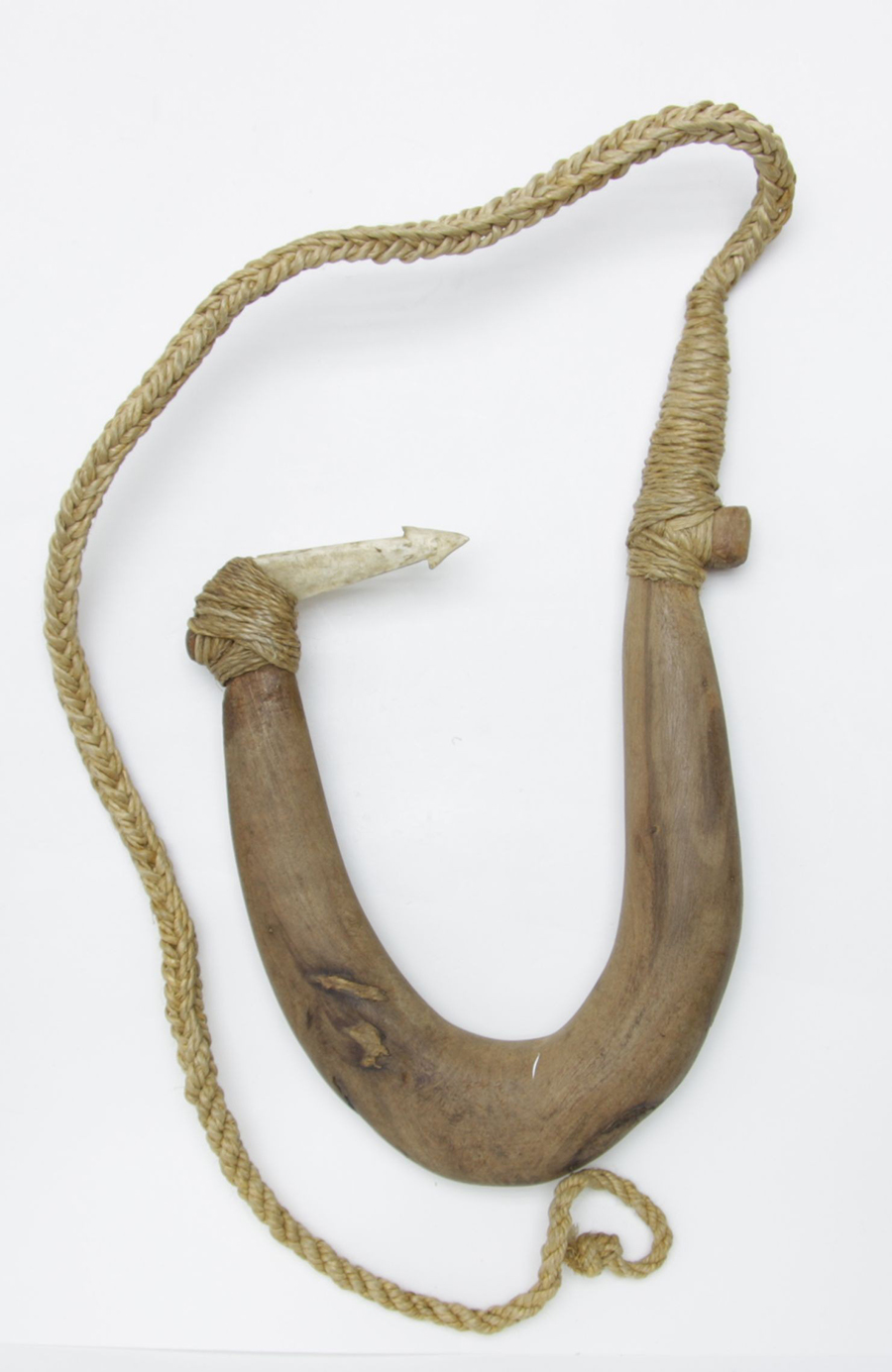 A bone fishhook carved with a pattern at one end and has a woven cord attached.