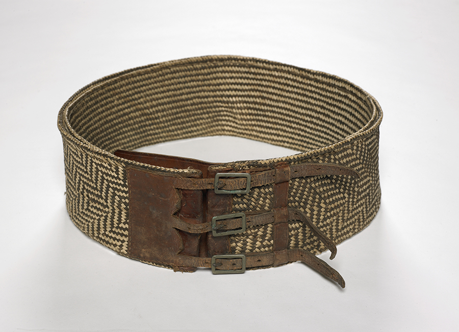 A woven belt sitting in a circle on a white surface. The belt is wide and has three buckles.