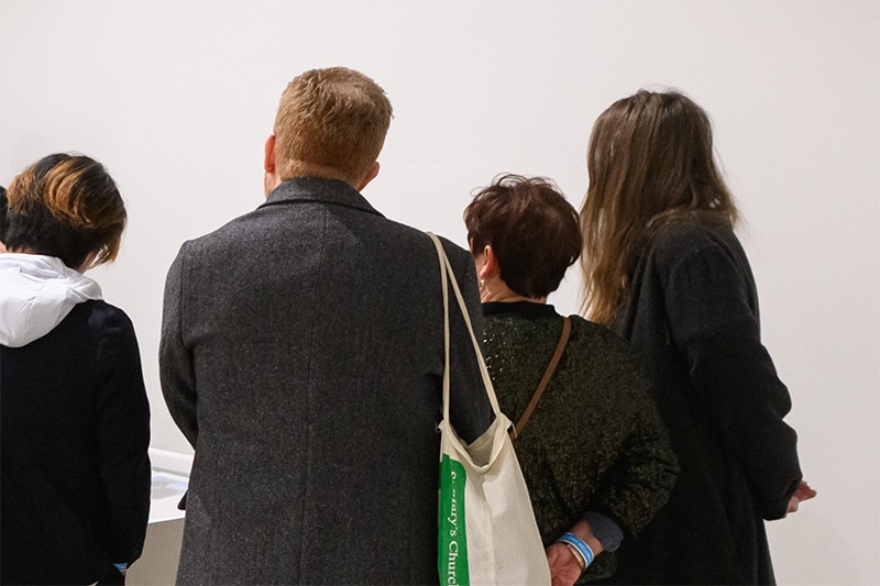 Four people with their backs to the camera are all looking at something out of view.