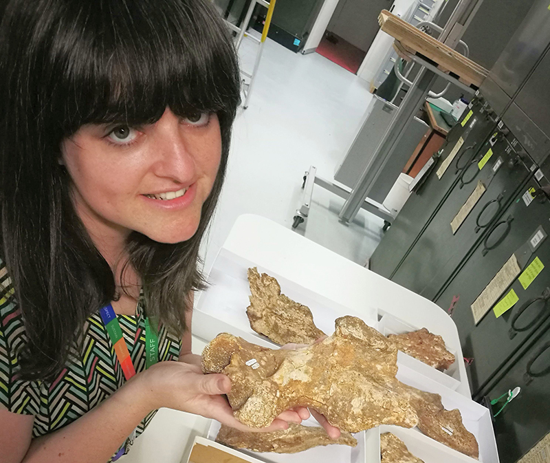 A woman is holding a fossil and looking at the camera