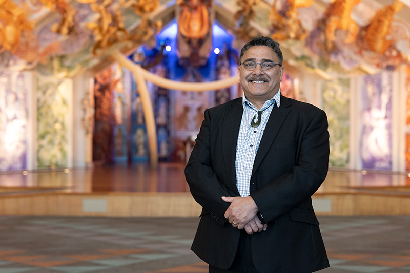 A man is standing in front of a colourful stage with his hands together in front of him.