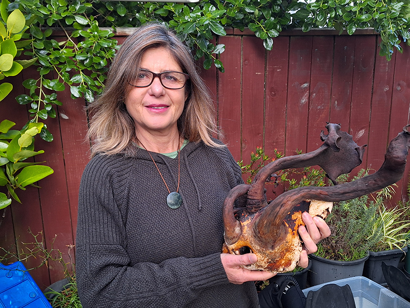 A woman is standing in a garden and holding a large piece of dried algae or seaweed.