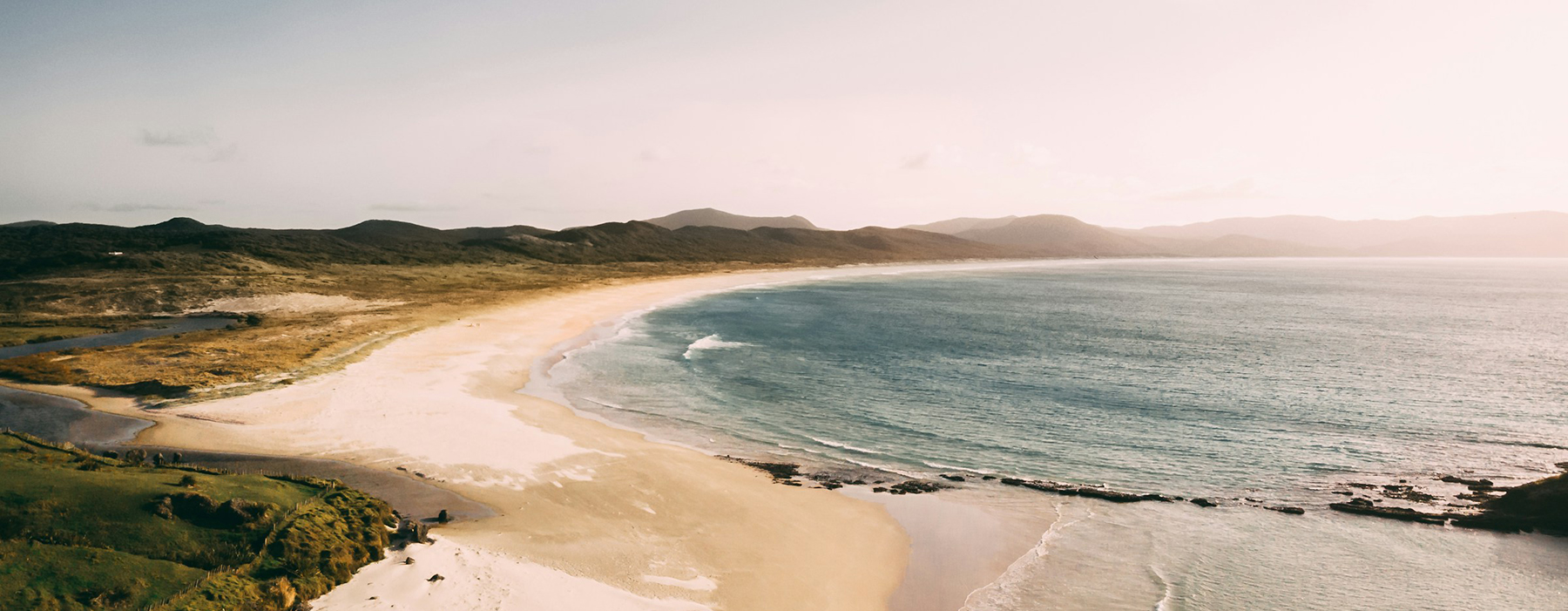 A photo of a long sandy beach with the sea lapping at the shore.