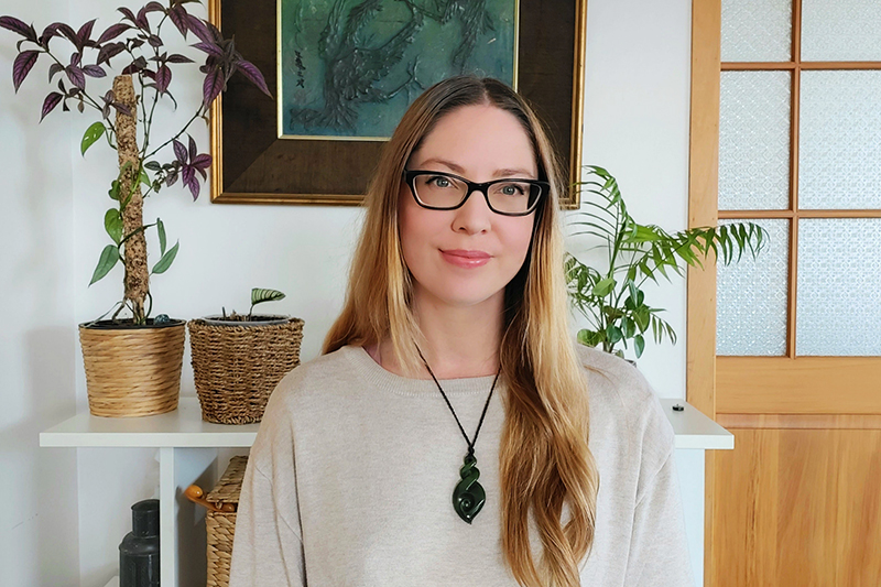 A woman with long blond hair and glasses is smiling serenely at the camera.