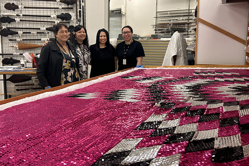 Four women stand together behind a very pink and sparkly quilt laid out on a drawer