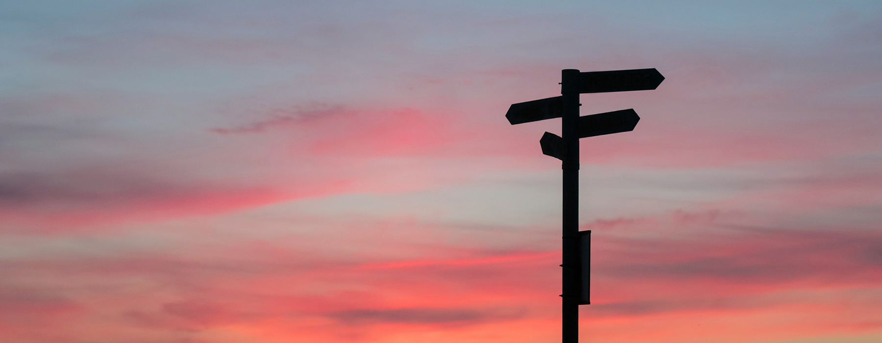 A roadsign with three different directions silhouetted against a sunset.