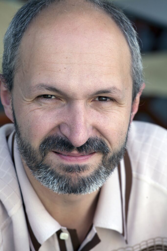 Head shot of a balding man with a short beard and moustache smiling at the camera.