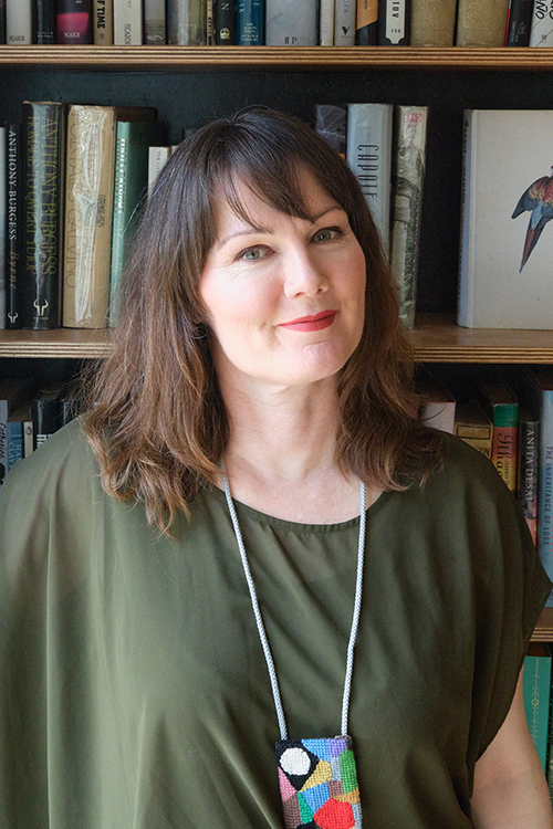 Head and shoulders of a woman with shoulder-length brown hair. She is standing in front of a bookcase.