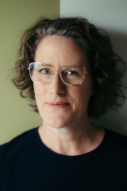 Head and shoulders of a woman wearing glasses and smiling at the camera.