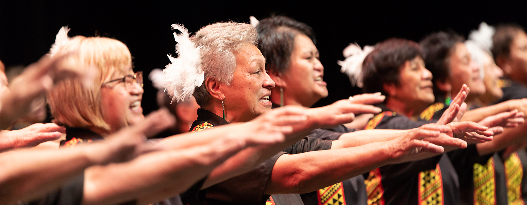 Several older women are performing on stage. They are all facing the same direction with their arms up at shoulder level.