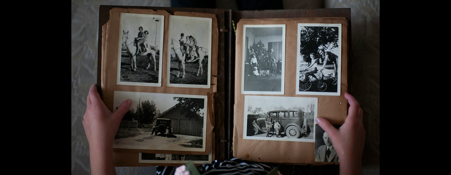 a top-down photo of an open photo album with six black and white photos of people in the page spread. There are two hands holding the album open.