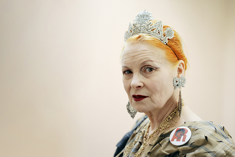 A long beige banner image with an older woman with bright orange hair, heavy makeup, a tiara and bold jewellery on. She is looking at the camera with a slight sneer.