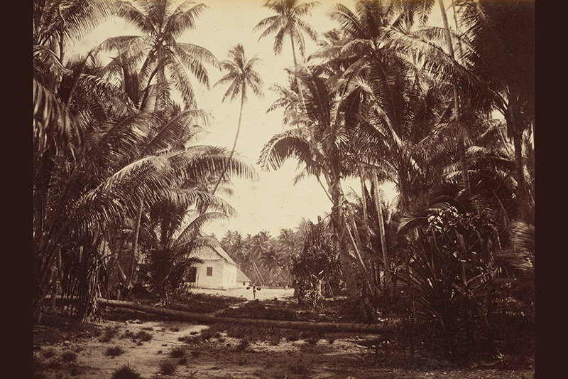 A sepia photo of a Pacific island with a small house or church in the background.