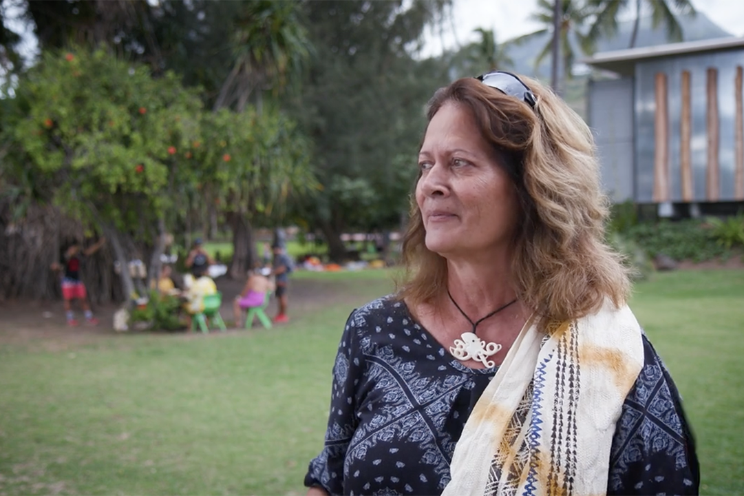 A woman with long hair is standing outside and looking off into the distance.