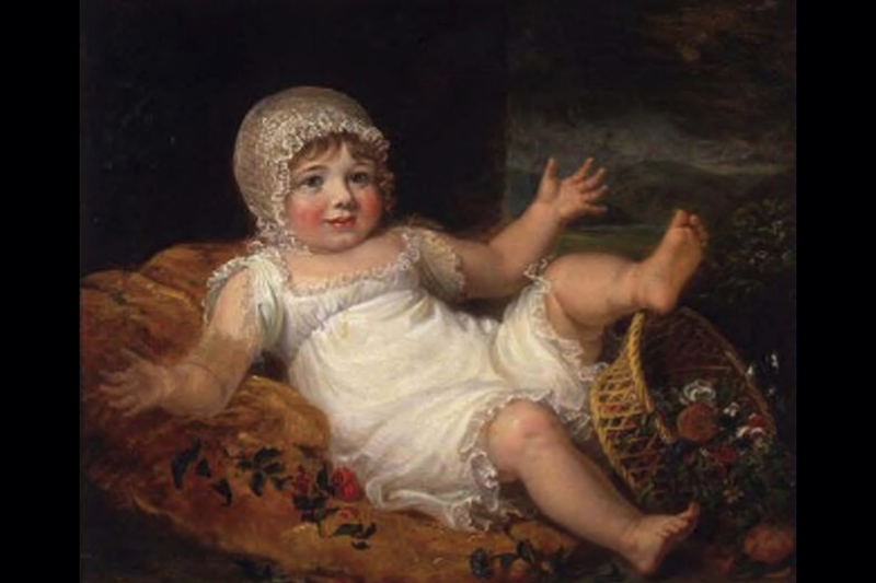 A young baby with a bonnet and white dress on is lying on its back with hands and one leg in the air.