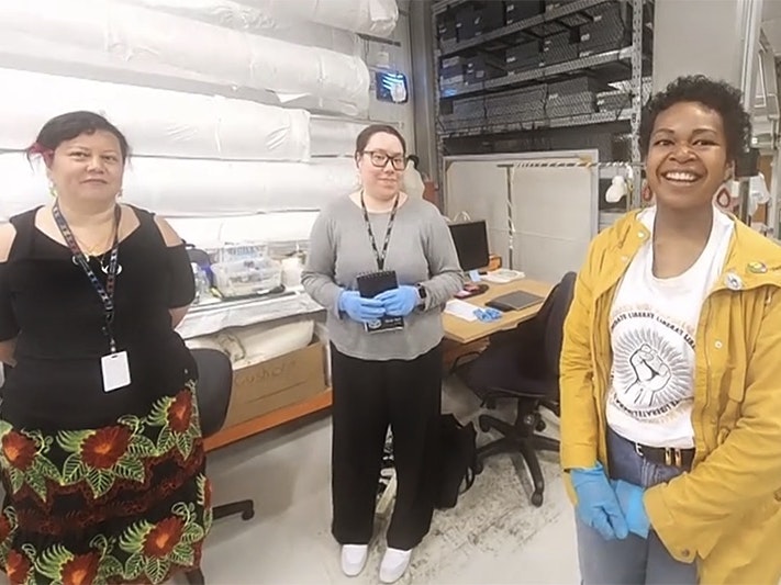Emelihter Kihleng, research student Melanie Ioane-Warren and Emele Ugavule. Te Papa Three women are standing in a museum storage room and smiling at the camera.