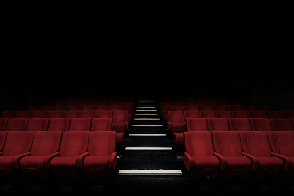 A dark, empty theatre with rows of red seats illuminated by dim lights on the steps 